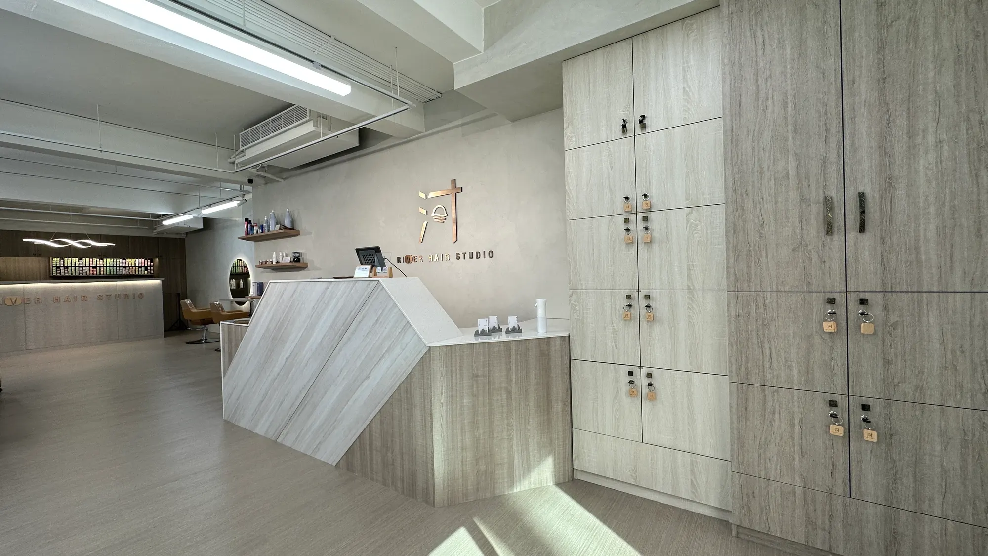河的店內:淺灰木紋櫃台、牆上的銅色河字 Logo 與置物櫃
